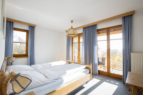 Bright hotel room at Landgasthof Bieg with twin beds, wooden frames, blue curtains, and large windows with balcony access