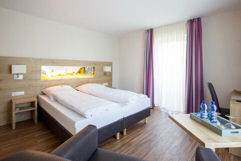 Bright hotel room at Landgasthof Bieg with two single beds, wooden headboard, bedside table, and chairs by a window with purple curtains