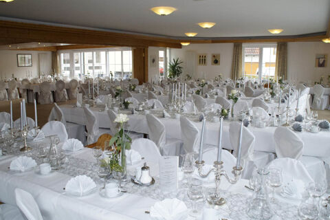 A large banquet hall at Landgasthof Bieg with white-covered chairs and tables set with folded napkins, candles, and glassware