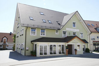 Light green building with multiple windows and flower pots outside the entrance of Landgasthof Bieg under a clear sky