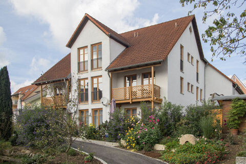 White multi-story building with brown roof and wooden balconies surrounded by a garden with colorful flowers at Landgasthof Bieg