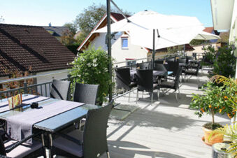 Outdoor patio seating with black wicker chairs, tables with umbrellas, and plants at Landgasthof Bieg