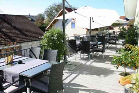 Outdoor patio seating with black wicker chairs, tables with umbrellas, and plants at Landgasthof Bieg