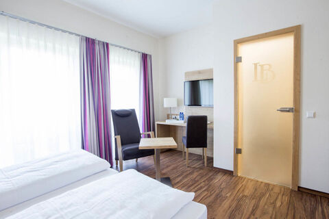Hotel room at Landgasthof Bieg with two beds, a black chair, wooden table, desk with TV, and frosted door with logo