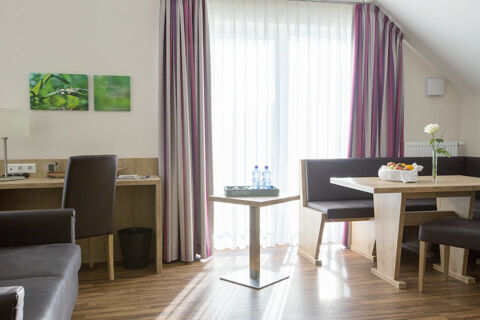 Bright hotel room at Landgasthof Bieg with wooden floors, desk, small table with water bottles, and dining area with fruit bowl and flower