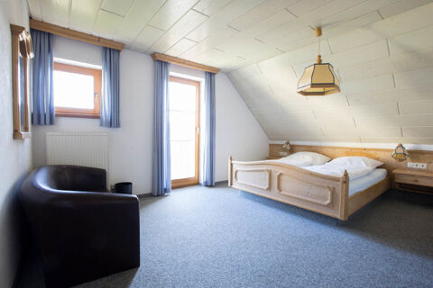 Bedroom at Landgasthof Bieg with wooden double bed, two bedside tables, blue curtains, an armchair, and carpeted floor