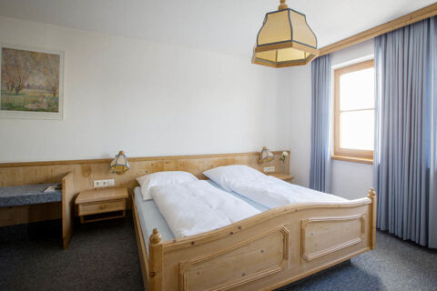 Bedroom at Landgasthof Bieg featuring a wooden double bed with white bedding, a window with blue curtains, and two nightstands