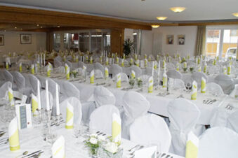 A banquet hall at Landgasthof Bieg with several long tables set with white cloths, white chairs, folded yellow-striped napkins, and glassware