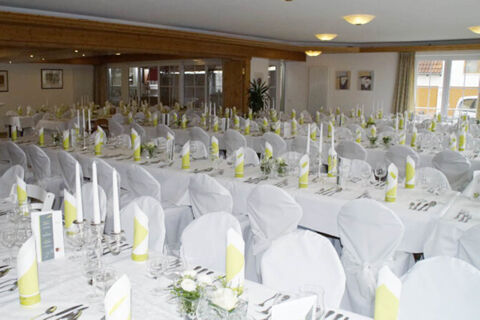 A banquet hall at Landgasthof Bieg with several long tables set with white cloths, white chairs, folded yellow-striped napkins, and glassware