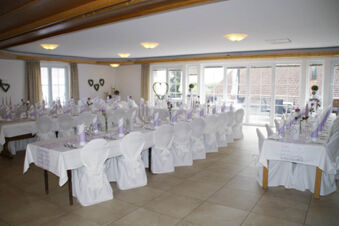 A banquet room at Landgasthof Bieg with white covered chairs and tables set with folded napkins and flowers by large windows