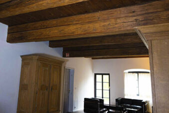 Room interior at Landgasthof Restaurant Adler with wooden ceiling beams, a wooden wardrobe, black armchairs, and a window with white curtains