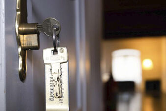 Key inserted in a brass lock on a white door with a metal keychain hanging in Landgasthof Restaurant Adler