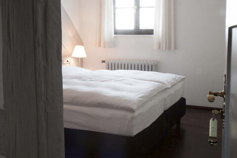Minimalistic hotel room at Landgasthof Restaurant Adler with a neatly made double bed, bedside lamp, and window with curtains