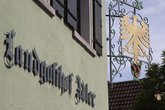 Metal sign with a golden eagle hangs on a green ornate bracket beside the building with Landgasthof Restaurant Adler text