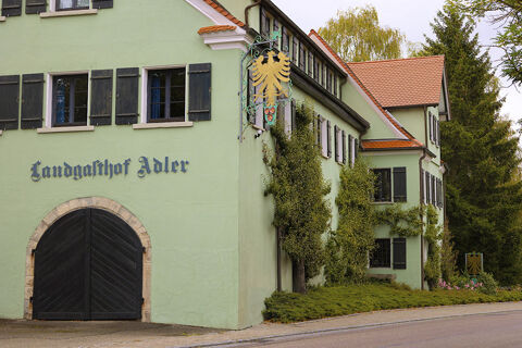 Green building with black shutters and arched black door with sign Landgasthof Restaurant Adler and golden eagle emblem