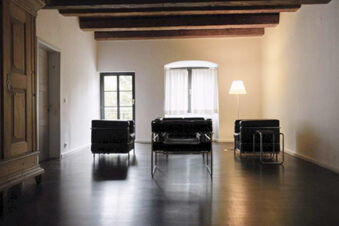Three black chairs, a wooden armoire, a floor lamp and two windows in a minimal lounge at Landgasthof Restaurant Adler