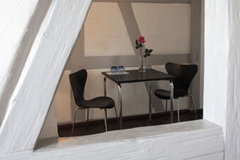 Two black chairs and a table with a glass vase holding a single pink rose inside Landgasthof Restaurant Adler