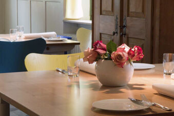 Close-up of a dining table at Landgasthof Restaurant Adler with pink roses in a white vase and tableware set up for guests