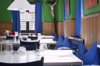 Dining area at Landgasthof Restaurant Adler with white tables, blue chairs, wooden wall paneling, and a crucifix on the wall
