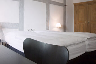 A minimalistic hotel room at Landgasthof Restaurant Adler with a neatly made bed, wooden wardrobe, and a lit bedside lamp