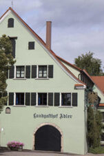Light green building with black shutters, arched black doors, and the name Landgasthof Restaurant Adler on the facade