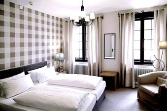 Alt N&uuml;rnberg Hotel 明亮的客房，配有兩張單人床、格子牆、兩扇窗戶、扶手椅和現代燈罩。