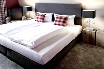 Alt N&uuml;rnberg 酒店的現代化客房，配有大型雙人床、格子墊、扶手椅和木方塊上的木質檯燈。