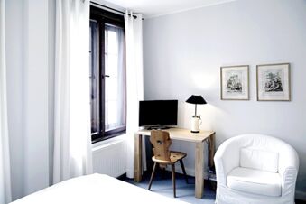 Alt N&uuml;rnberg Hotel 明亮、裝潢簡潔的客房，配有木桌、電視和舒適的白色扶手椅。