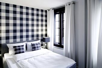 Alt N&uuml;rnberg Hotel 現代化的飯店客房，配備舒適的床、棋盤格牆面圖案，以及裝有白色窗簾的窗戶。