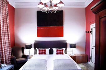 Alt N&uuml;rnberg Hotel 明亮的臥室配有雙人床、格子墊子和窗簾以及扶手椅。