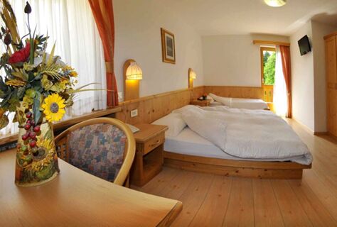 &Uacute;tuln&yacute; dvoulůžkov&yacute; pokoj v hotelu Albergo Nido Verde s dřevěn&yacute;m obložen&iacute;m, dvěma postelemi, balkonem a dekorativn&iacute; květinovou v&yacute;zdobou na stole.