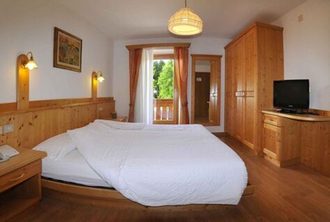 Světl&yacute; pokoj s manželskou postel&iacute;, dřevěn&yacute;m n&aacute;bytkem a balkonem s v&yacute;hledem do zeleně v hotelu Albergo Nido Verde.