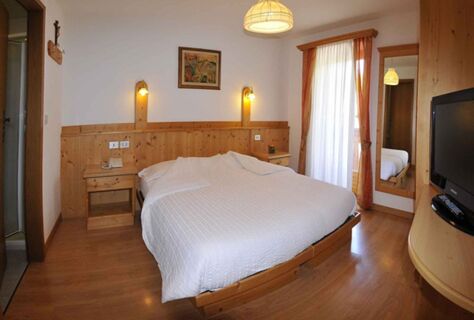 &Uacute;tuln&yacute; dvoulůžkov&yacute; pokoj v hotelu Albergo Nido Verde s dřevěn&yacute;m n&aacute;bytkem, velkou postel&iacute;, nočn&iacute;mi stolky a balkonem se z&aacute;věsy.