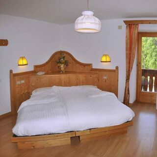 Světl&aacute; ložnice s dřevěn&yacute;m n&aacute;bytkem a velkou postel&iacute; v hotelu Albergo Nido Verde, s balkonem a v&yacute;hledem do zeleně, pokoj osvětluj&iacute; dvě nočn&iacute; lampičky.