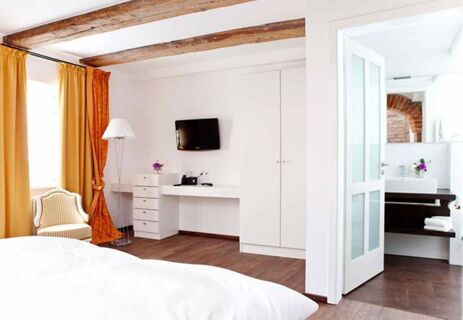 A hotel room at Brauereigasthof und Hotel Kapplerbr&auml;u featuring white walls, wooden ceiling beams, mustard curtains, a TV, wardrobe, and a view into the bathroom with flowers