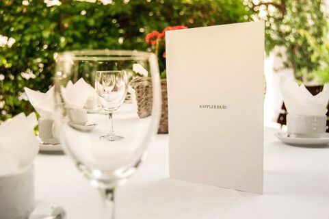 White menu card with Kapplerbr&auml;u text on a table set with wine glasses and napkins at Brauereigasthof und Hotel Kapplerbr&auml;u
