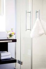 Bright bathroom interior with glass shower door, white towels, flowers, and dark countertop at Brauereigasthof und Hotel Kapplerbr&auml;u