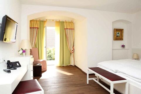 Bright hotel room at Brauereigasthof und Hotel Kapplerbr&auml;u with wooden floor, white walls, double bed, bench, and curtains