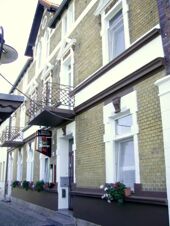 Die historische Fassade des Hotel-Pension Loreley mit hellbraunen Ziegeln, wei&szlig;en Fensterrahmen und dekorativen Balkonbr&uuml;stungen.