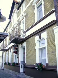 Die historische Fassade des Hotel-Pension Loreley mit hellbraunen Ziegeln, wei&szlig;en Fensterrahmen und dekorativen Balkonbr&uuml;stungen.