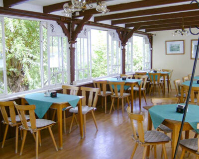 Hell und gem&uuml;tlich eingerichteter Speiseraum mit Holzm&ouml;beln und gro&szlig;en Fenstern im Hotel-Pension Loreley mit Blick ins Gr&uuml;ne.