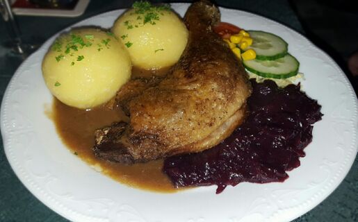 Ein Teller mit gebratenem H&auml;hnchenschenkel, Kartoffelkn&ouml;deln, Rotkohl, Salat und So&szlig;e im Hotel-Pension Loreley serviert.