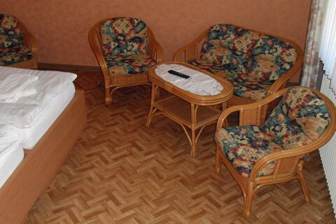 A seating area with floral patterned cushions including two armchairs and a loveseat around a wicker coffee table with a remote at Hotel garni Zur Krim