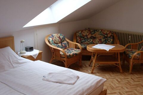 Accogliente camera d'albergo con lucernario inclinato, mobili in rattan e letto dell'Hotel garni Zur Krim per un soggiorno rilassante.