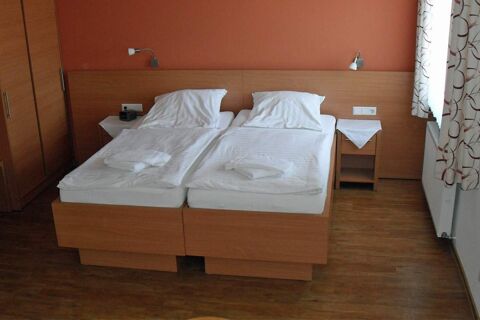 Ein schlicht eingerichtetes Doppelzimmer mit zwei Betten und Holzm&ouml;beln im Hotel garni Zur Krim mit Fenstervorhang und Nachttischen.
