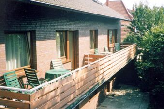 Balkon mit gr&uuml;nen St&uuml;hlen und Tischen an einer Backsteinfassade des Hotel garni Zur Krim, umgeben von B&auml;umen.