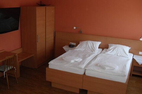 Hotel garni Zur Krim room with two single beds pushed together, wooden furniture, wall-mounted TV, and orange walls