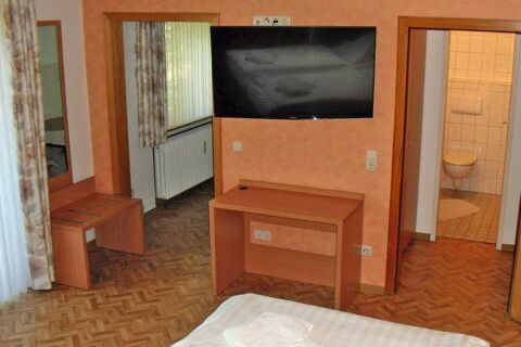 Hotel garni Zur Krim room with wooden desk, wall-mounted TV, small stool, bed with white linens, and door to tiled bathroom