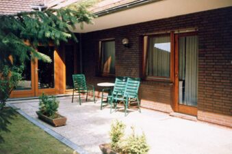 Sonnige Terrasse mit gr&uuml;nen St&uuml;hlen und Tischen vor dem Geb&auml;ude des Hotel garni Zur Krim mit braunen Ziegeln und Holzrahmenfenstern.