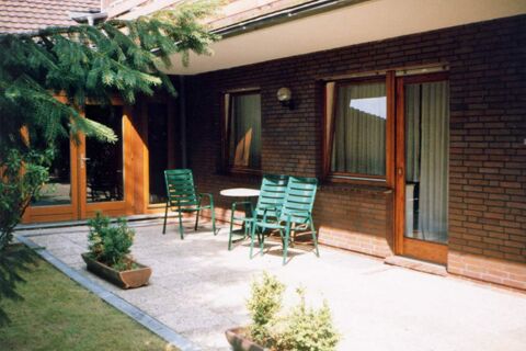 Sonnige Terrasse mit gr&uuml;nen St&uuml;hlen und Tischen vor dem Geb&auml;ude des Hotel garni Zur Krim mit braunen Ziegeln und Holzrahmenfenstern.